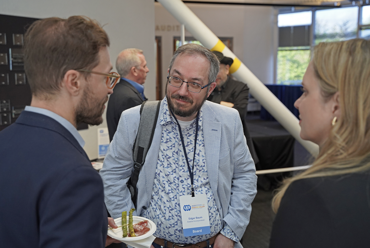 Three attendees of the Silicon Valley Deal Machine network and eat hors d’eouvres. This event, hosted by the Silicon Valley Chapter, brought together over 110 innovation leaders, IP professionals, and business dealmakers at the Computer History Museum in Mountain View, California. The middle man has a name tag that says Edgar Baum.